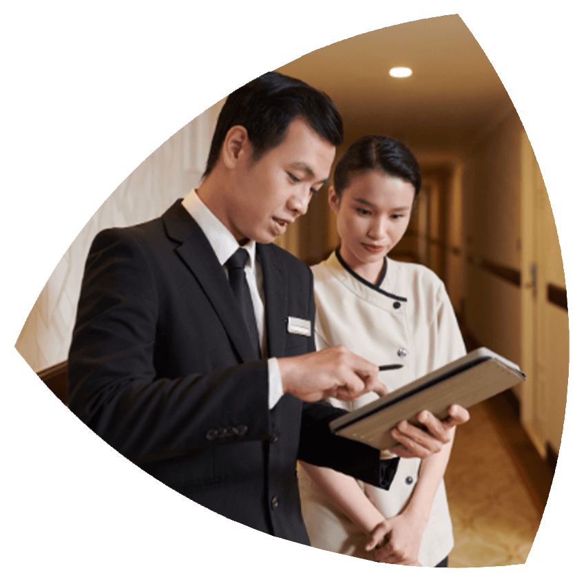 Supervisor de hotel revisando información en una tableta junto a una empleada en un pasillo del establecimiento.